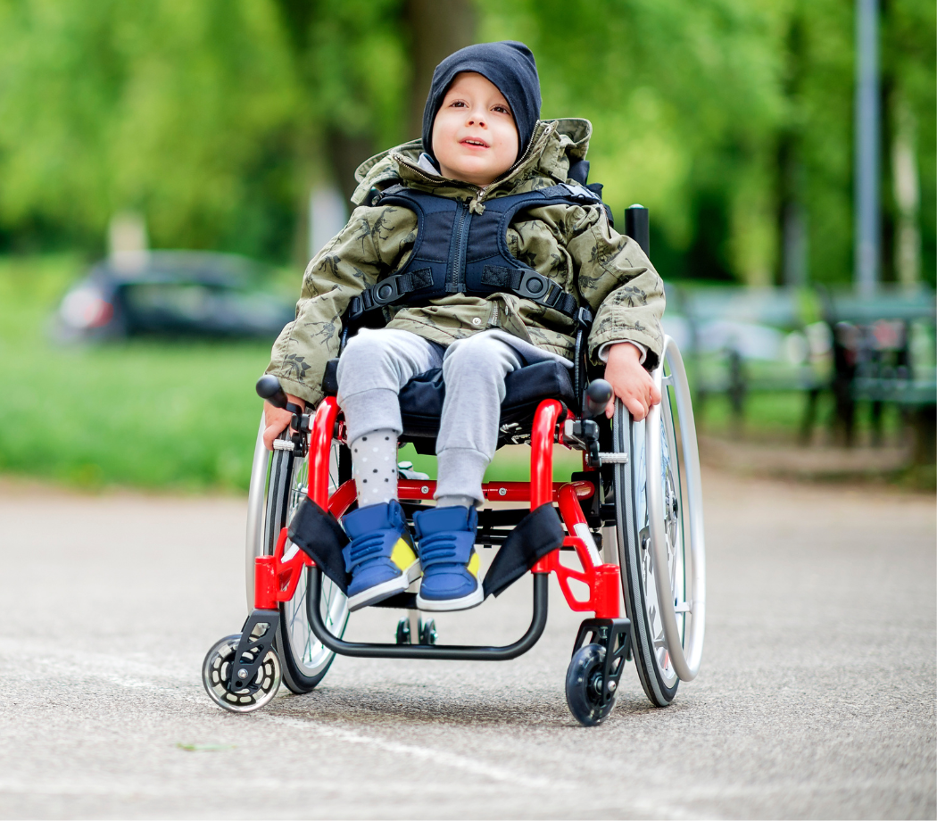 Child with disabilities, a wheelchair user, outside on a paved courtyard.